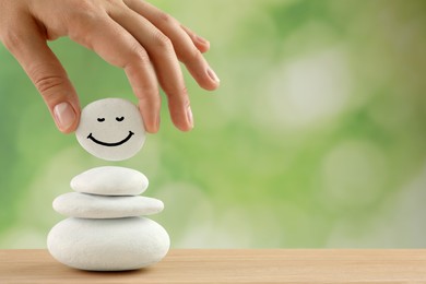 Woman putting stone with drawn happy face on stack against blurred green background, closeup and space for text. Zen concept