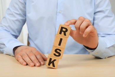Businessman destroying tower of cubes with word Risk at table, closeup