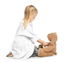 Cute child imagining herself as doctor while playing with stethoscope and toy bunny on white background
