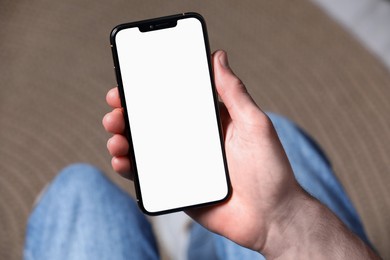 Photo of Man holding smartphone with blank screen indoors, closeup. Mockup for design