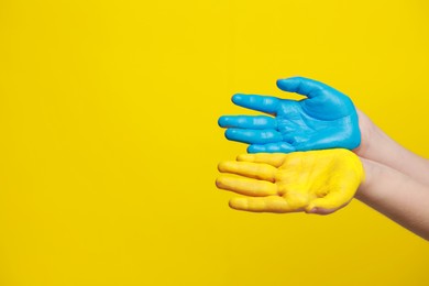 Little boy with hands painted in Ukrainian flag colors on yellow background, closeup and space for text. Love Ukraine concept