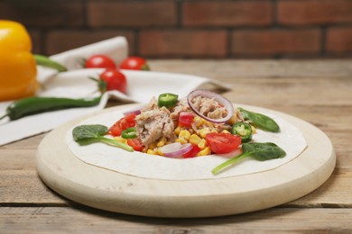 Photo of Delicious tortilla with tuna and vegetables on wooden table. Cooking shawarma