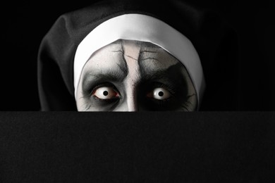 Scary devilish nun hiding on black background, closeup. Halloween party look