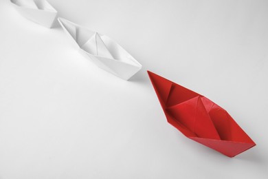 Photo of Paper boats following red one on white background, above view. Leadership concept