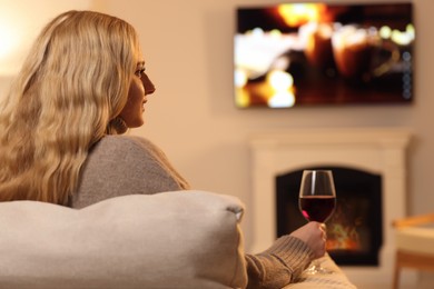 Beautiful young woman with glass of wine resting near fireplace at home