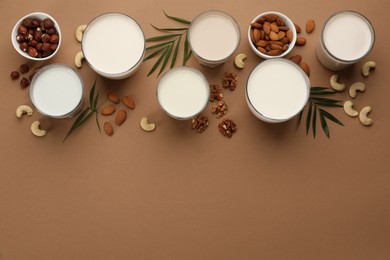 Different vegan milks and nuts on brown background, flat lay. Space for text