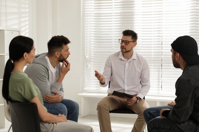 Psychotherapist working with group of drug addicted people at therapy session indoors