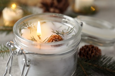 Burning scented conifer candle in glass jar, closeup view