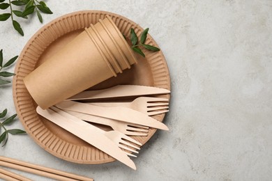 Disposable tableware and green twigs on light background, flat lay. Space for text