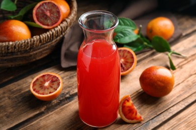 Photo of Tasty sicilian orange juice in glass bottle and fruits on wooden table