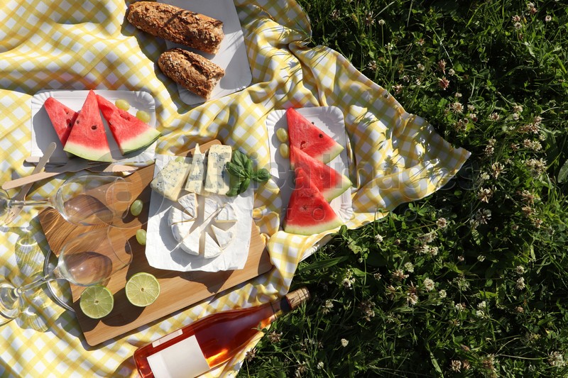 Picnic blanket with delicious food and wine on green grass outdoors, top view