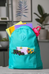 Turquoise backpack with different school stationery on table indoors