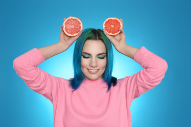 Young woman with bright dyed hair holding grapefruit on light blue background