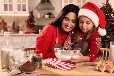 Happy mother and her daughter making dough for Christmas cookies at home
