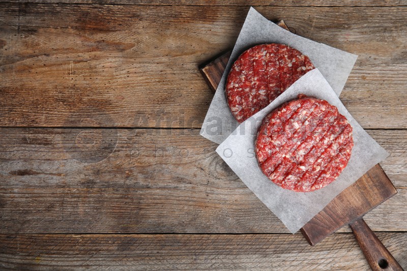 Raw meat cutlets for burger on wooden table, top view. Space for text