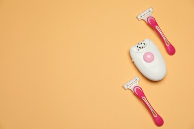 Modern epilator and razors on orange background, flat lay. Space for text