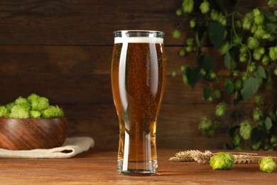 Photo of Glass of beer, fresh green hops and spikes on wooden table