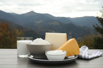 Tasty cottage cheese and other fresh dairy products on grey wooden table in mountains