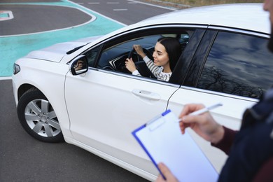 Instructor near car with his student during exam at driving school test track