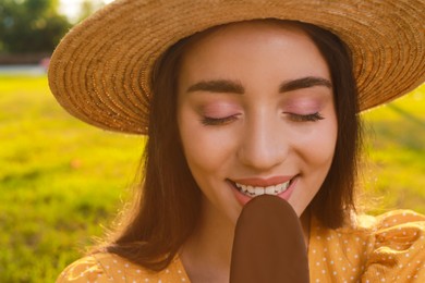 Beautiful young woman eating ice cream glazed in chocolate outdoors, closeup