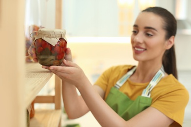 Woman putting jar of pickled vegetables on shelf indoors