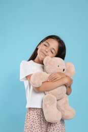 Cute girl wearing pajamas with teddy bear on light blue background