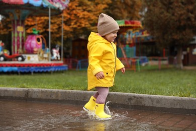 Photo of Cute little girl walking in puddle outdoors on rainy weather