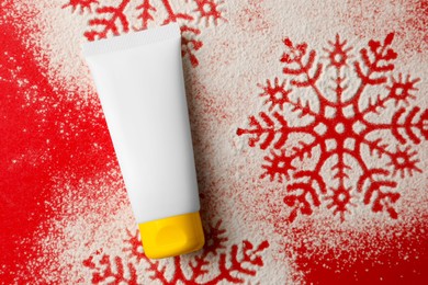 Photo of Winter skin care. Hand cream and snowflake silhouettes made with artificial snow on red background, top view