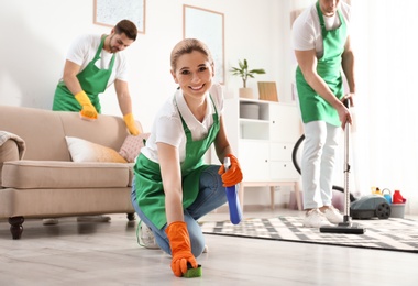 Woman using sponge and detergent for floor cleaning with her team in living room