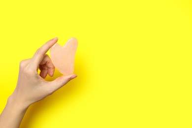 Photo of Woman with rose quartz gua sha tool on yellow background, closeup. Space for text