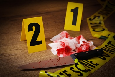 Knife, bloody napkin and crime scene markers on wooden table