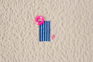 Striped beach towel, flip flops and swim ring on sand, aerial view