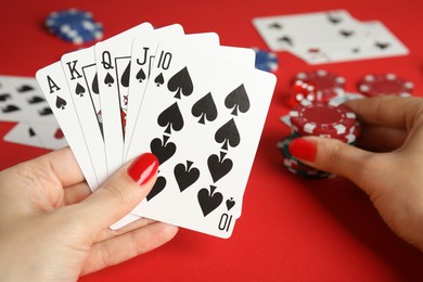 Woman holding playing cards with royal flush combination and poker chips at red table, closeup