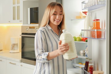 Young woman with gallon of milk near refrigerator in kitchen