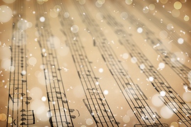 Old sheet with Christmas music notes as background, snowflakes and bokeh effect