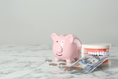Educational dental typodont model, piggy bank and money on white marble table, space for text. Expensive treatment