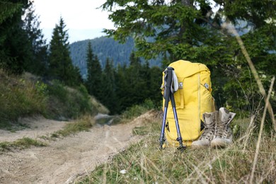 Photo of Backpack, trekking poles and boots outdoors, space for text. Tourism equipment