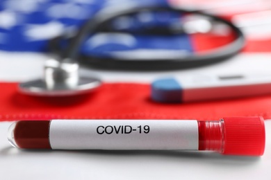 Test tube with blood sample and stethoscope on American flag, closeup. Coronavirus pandemic in USA