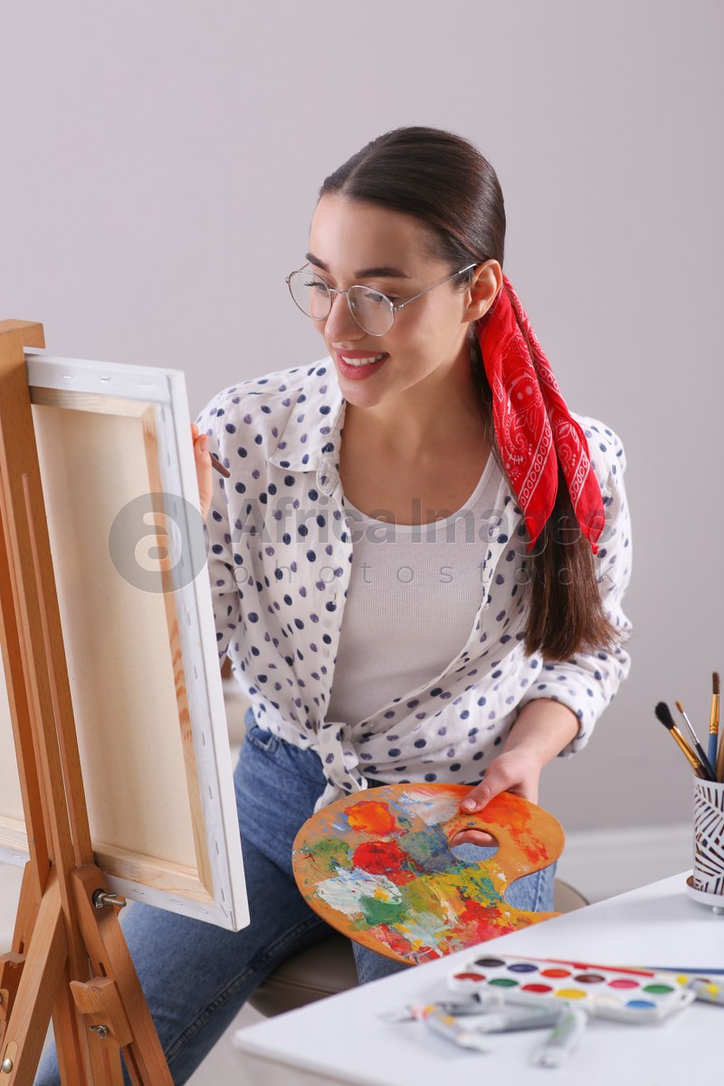 Happy woman artist drawing picture on canvas indoors