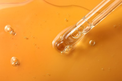 Dripping hydrophilic oil from pipette on orange background, closeup