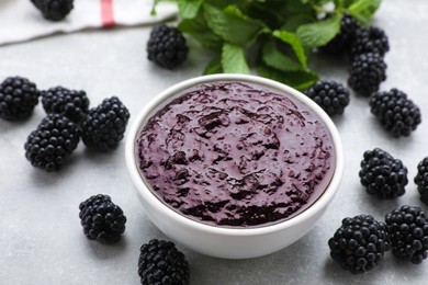 Blackberry puree in bowl and fresh berries on light grey table, closeup
