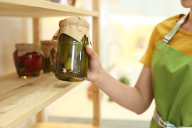 Woman putting jar of pickles on shelf indoors, closeup
