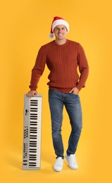 Man in Santa hat with synthesizer on yellow background. Christmas music