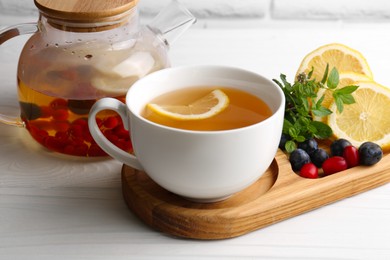 Cup with delicious immunity boosting tea and ingredients on white wooden table, closeup