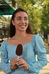 Beautiful young woman holding ice cream glazed in chocolate on city street