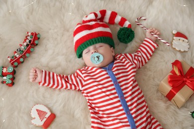 Cute little baby with Christmas candy cane sleeping on fluffy blanket, view from above