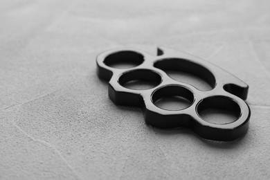 Black brass knuckles on grey stone background, closeup. Space for text