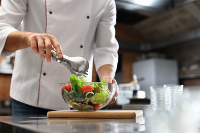 Photo of Professional chef making salad in restaurant kitchen, closeup