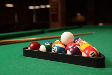 Photo of Plastic triangle rack with billiard balls and cue on green table indoors, space for text