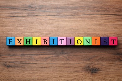 Word EXHIBITIONIST made with colorful cubes on wooden table, flat lay